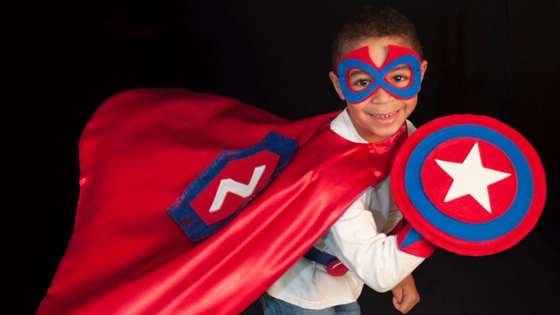 Young boy wearing red and blue superhero cape