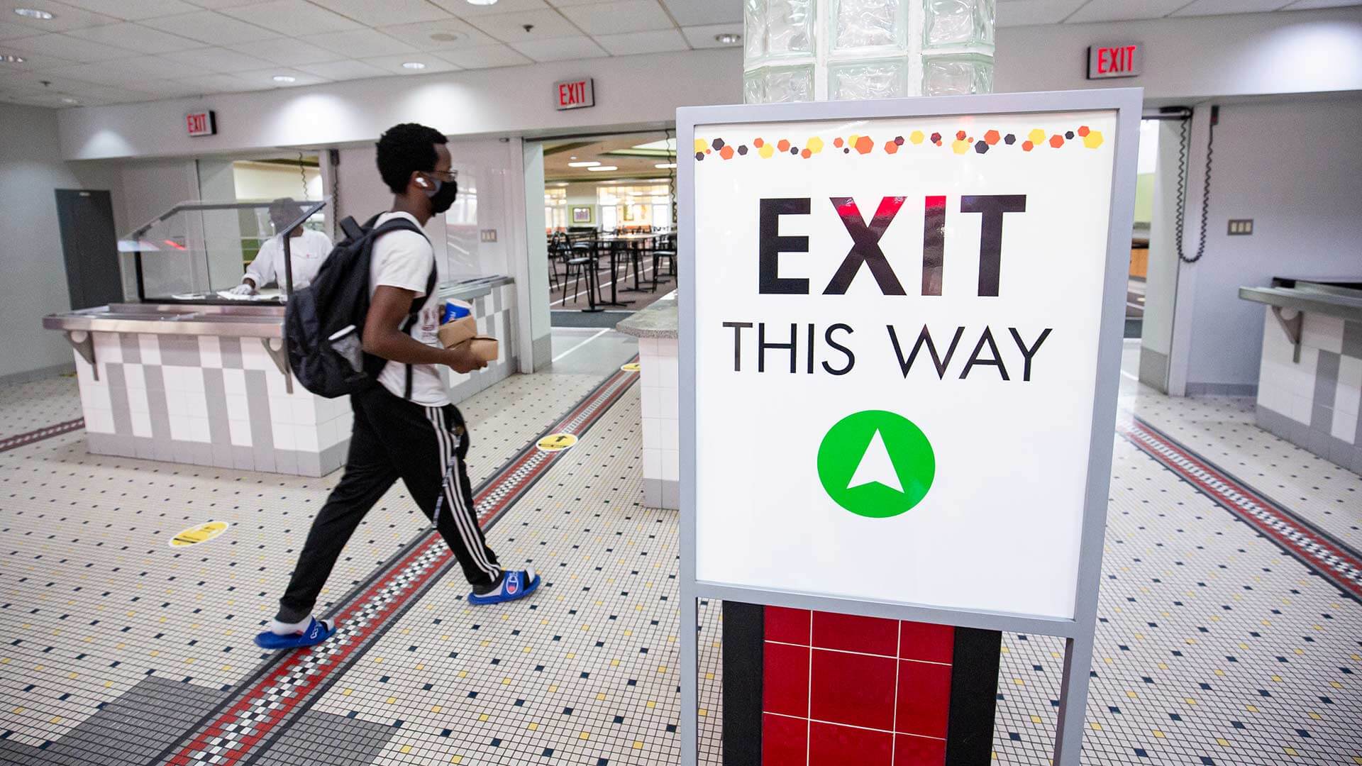 Student walking by "Exit this way" sign in dining hall